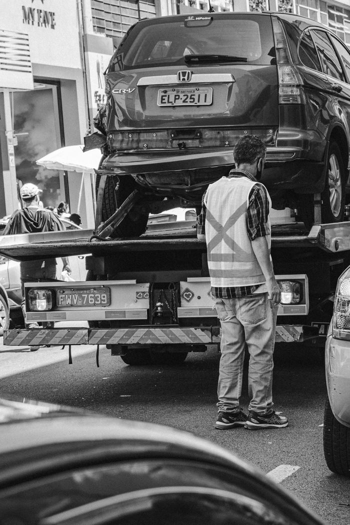 services-03 Grayscale image of a tow truck loading a vehicle on a busy street in São Paulo.