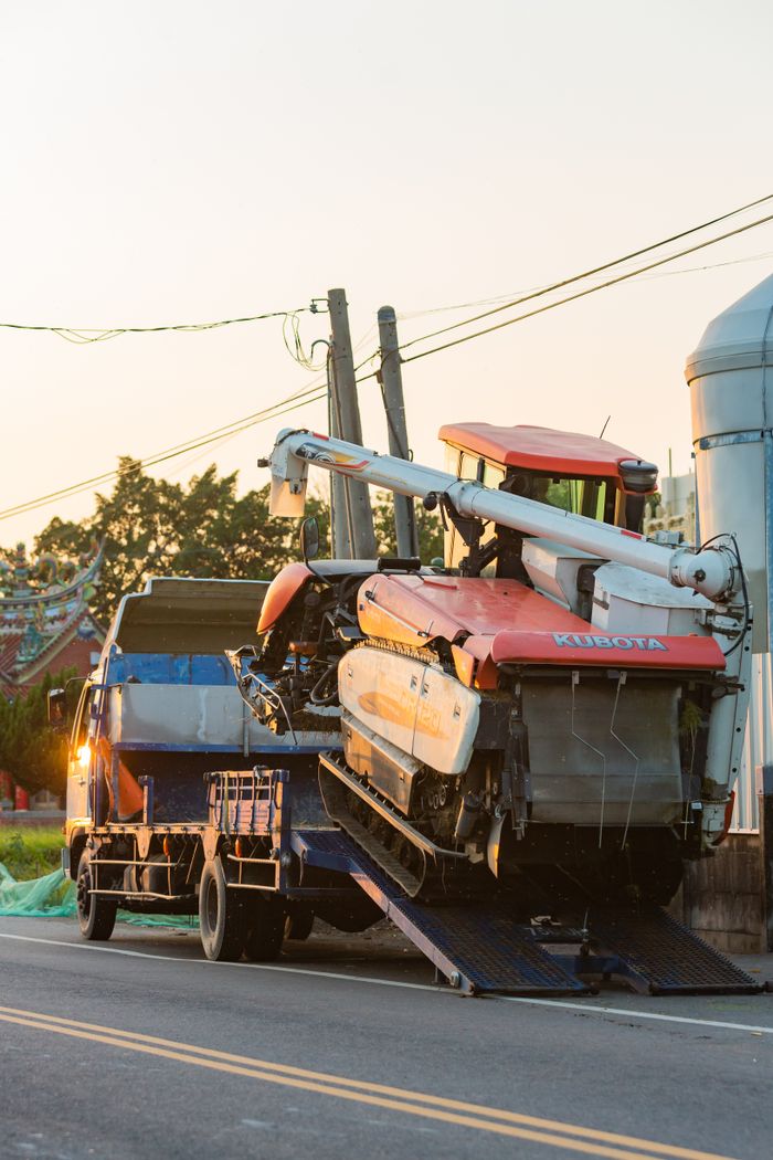gallery-4 Orange excavator being loaded onto a truck in a rural setting during daytime.