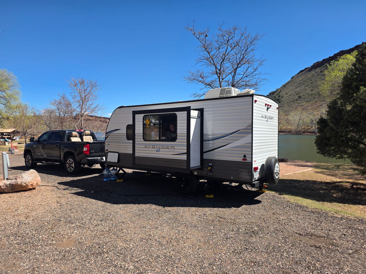 gallery-2 A scenic daytime camping setup with a caravan and truck by a lake in a natural setting.