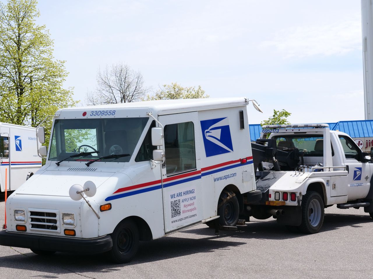 about-01 A United States Postal Service (USPS) mail truck is being towed outdoors on a clear day.