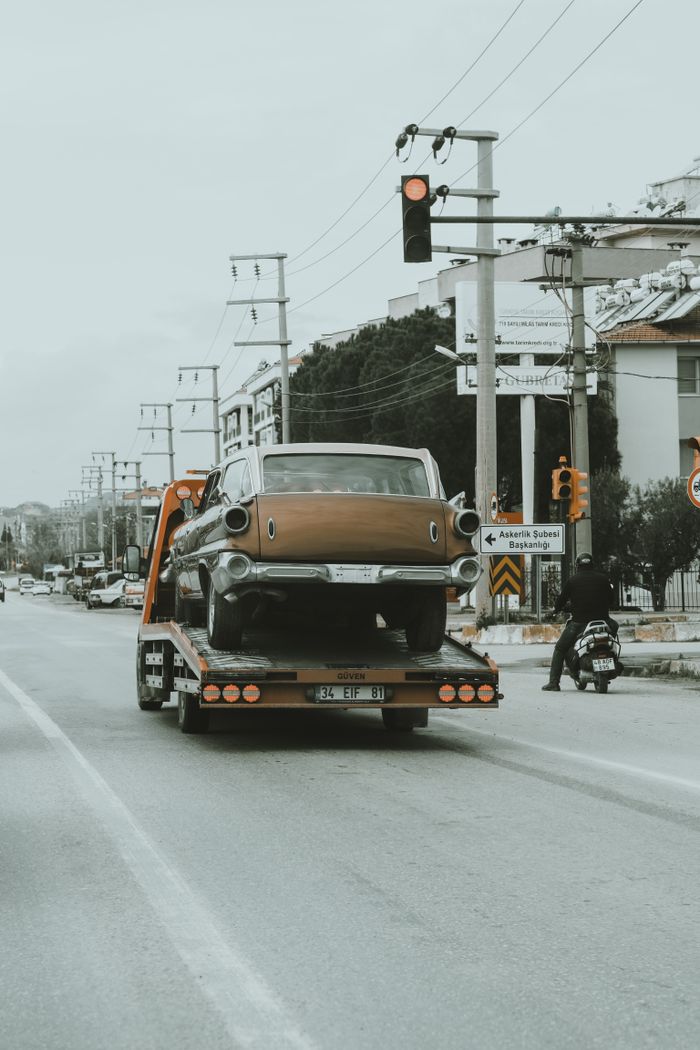 why-choose-us A vintage car is being towed through city streets on a tow truck, showcasing an urban environment.